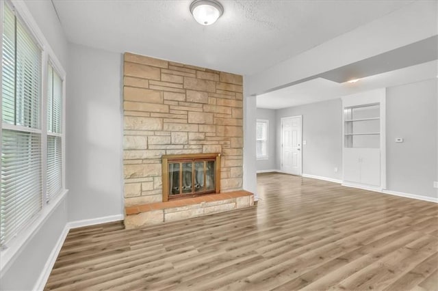 315 S Crane St S, Independence, MO 64050 - unfurnished living room with wood finished floors, a textured ceiling, baseboards, and a stone fireplace