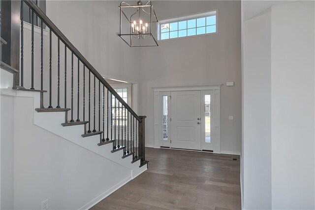 entrance foyer featuring a towering ceiling, a chandelier, wood finished floors, stairway, and baseboards
