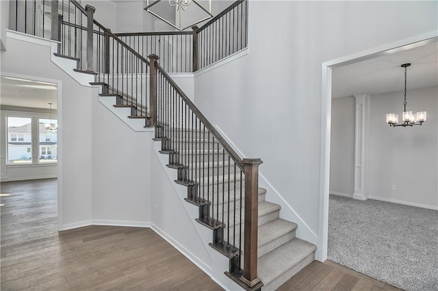 stairway featuring a chandelier, wood finished floors, a towering ceiling, and baseboards