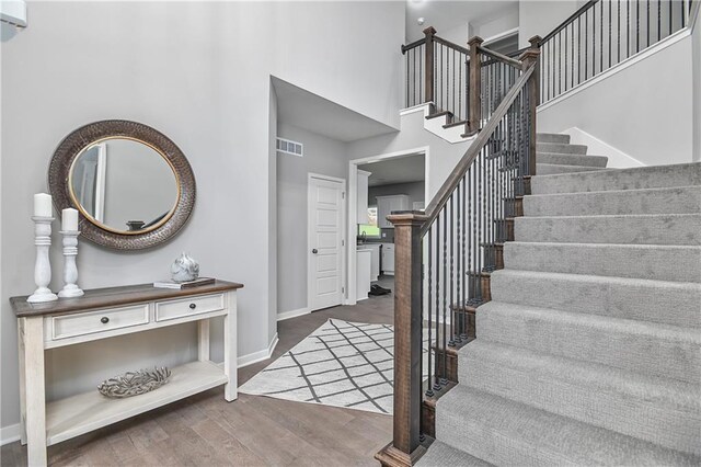 foyer entrance with stairway, wood finished floors, a towering ceiling, and baseboards