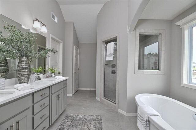 bathroom featuring a soaking tub, double vanity, a stall shower, and baseboards