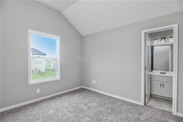 unfurnished bedroom featuring light colored carpet, vaulted ceiling, baseboards, a sink, and connected bathroom