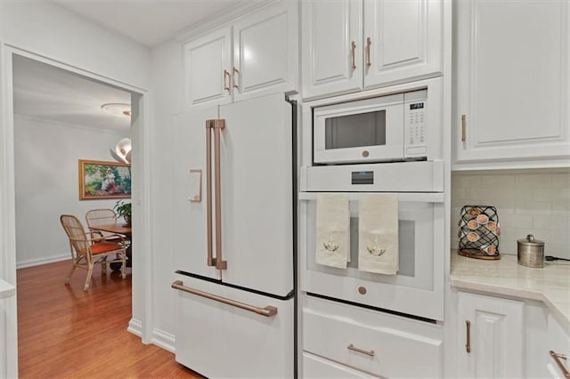 kitchen with white appliances, decorative backsplash, white cabinetry, and light wood-type flooring