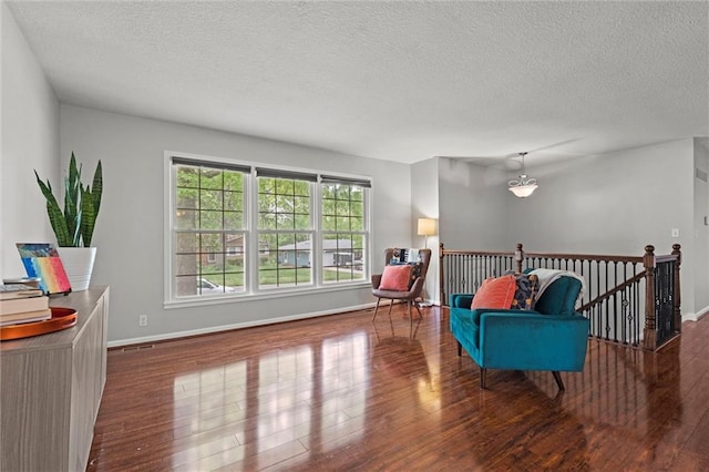 living area featuring wood finished floors, a textured ceiling, baseboards, and an upstairs landing