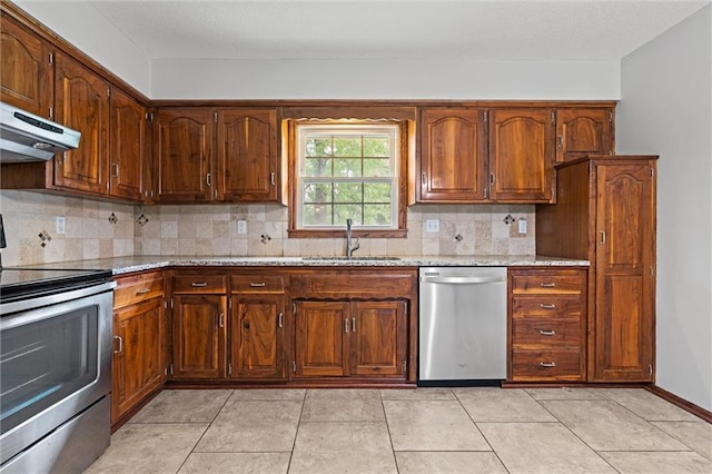 kitchen with stainless steel appliances, a sink, under cabinet range hood, decorative backsplash, and light stone countertops