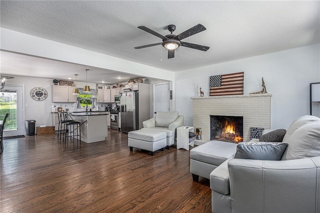 6405 Haskell Ave, Kansas City, KS 66104 - living room featuring dark wood-type flooring, ceiling fan, plenty of natural light, a fireplace, and a textured ceiling