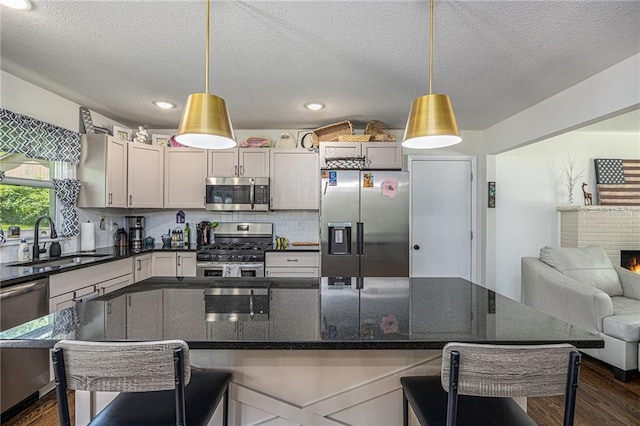 6405 Haskell Ave, Kansas City, KS 66104 - kitchen with appliances with stainless steel finishes, a sink, dark wood finished floors, a breakfast bar area, and a textured ceiling