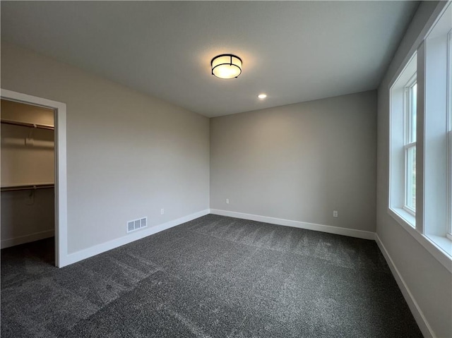 unfurnished bedroom with dark carpet, a walk in closet, baseboards, and recessed lighting