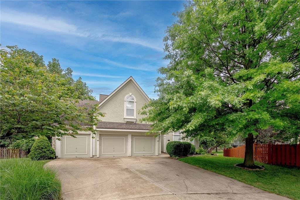 12565 Wedd St, Overland Park, KS 66213 - view of property hidden behind natural elements with stucco siding, concrete driveway, an attached garage, and roof with shingles