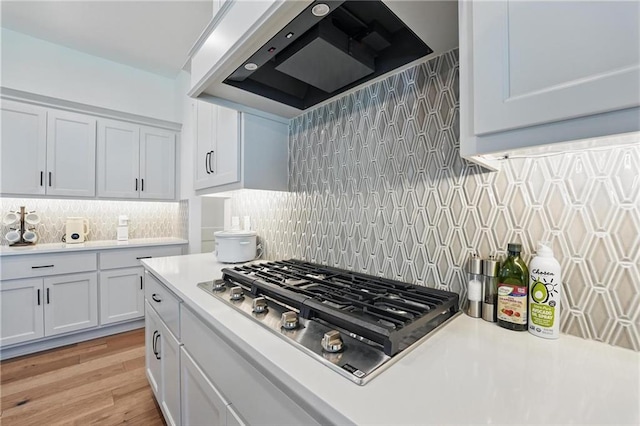 24765 W 89th Ter, Lenexa, KS 66227 - kitchen with wall chimney exhaust hood, stainless steel gas cooktop, light countertops, tasteful backsplash, and light wood-style flooring