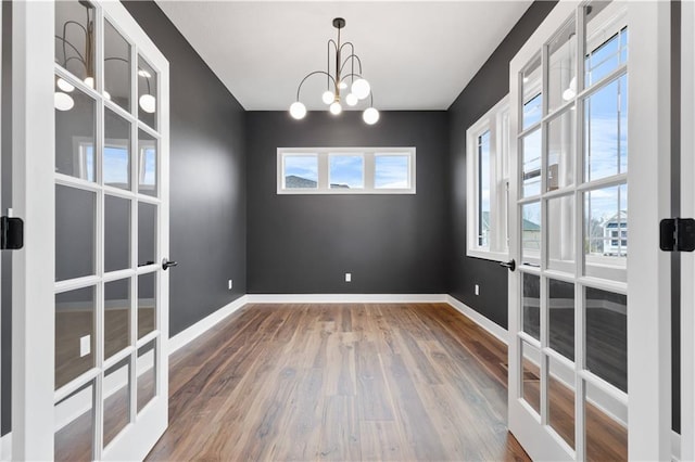 spare room with french doors, wood finished floors, plenty of natural light, and a chandelier