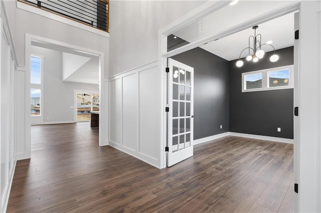 empty room with dark wood-type flooring, plenty of natural light, a chandelier, a towering ceiling, and baseboards