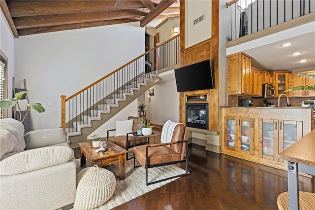 living area featuring stairway, dark wood finished floors, a high ceiling, beamed ceiling, and recessed lighting