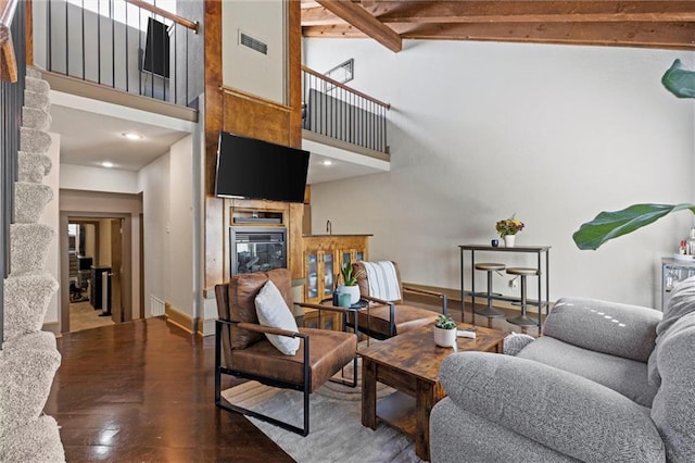 living room with a glass covered fireplace, a towering ceiling, baseboards, wood finished floors, and beam ceiling