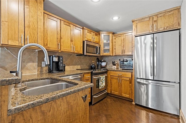 kitchen featuring stainless steel appliances, a sink, dark wood finished floors, brown cabinetry, and dark stone counters