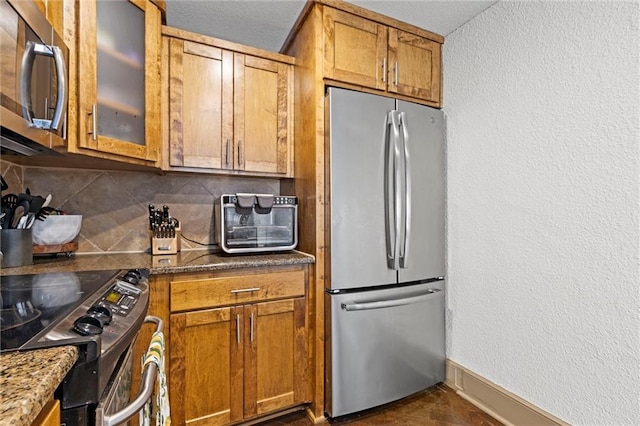 kitchen featuring stainless steel appliances, decorative backsplash, brown cabinetry, glass insert cabinets, and a textured wall