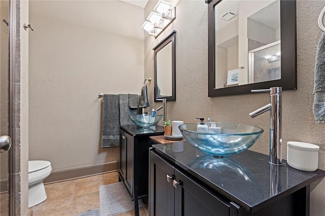 bathroom with vanity, a textured wall, a stall shower, baseboards, and toilet