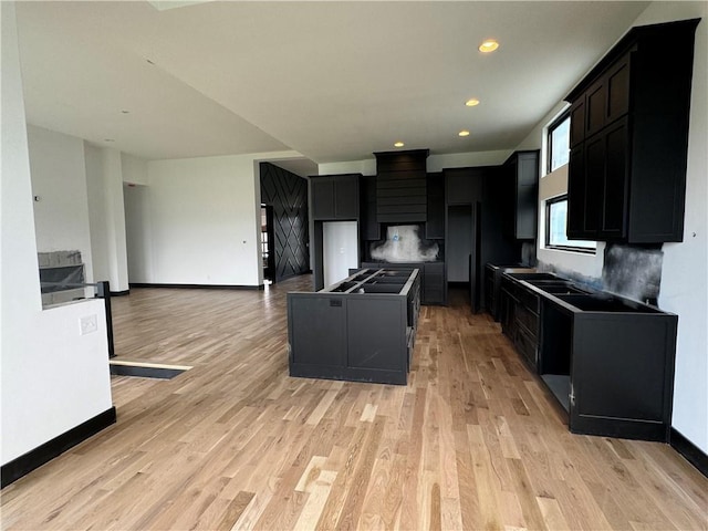 22659 W 87th St, Lenexa, KS 66227 - kitchen with light wood-type flooring, dark cabinetry, wall chimney exhaust hood, a kitchen island, and recessed lighting