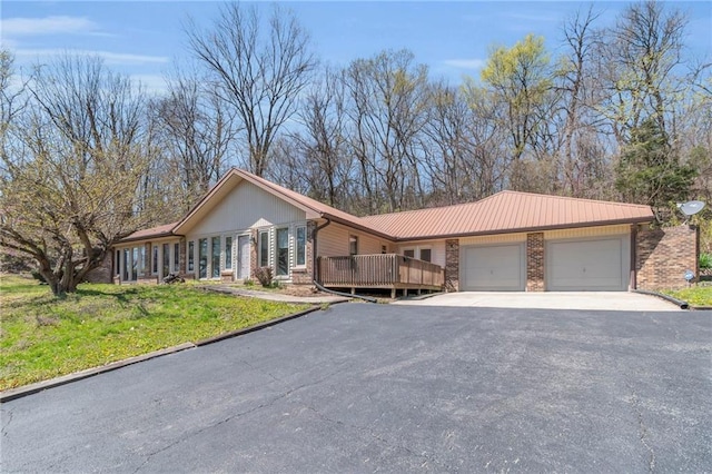 single story home with an attached garage, brick siding, asphalt driveway, a front lawn, and metal roof