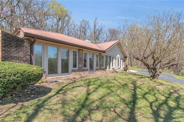 back of property featuring brick siding, a lawn, and metal roof
