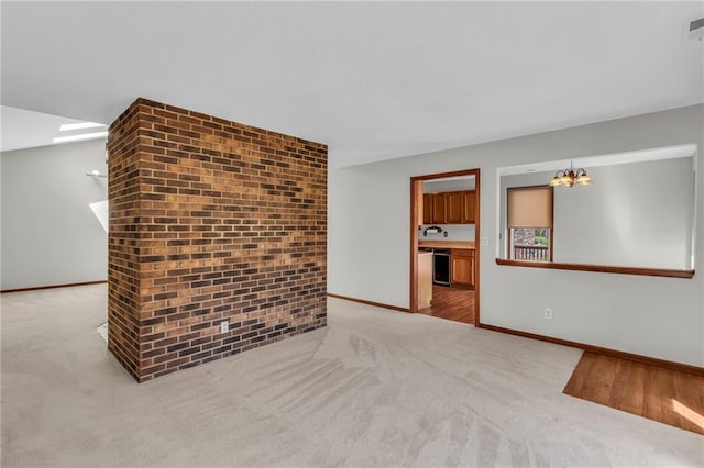 unfurnished living room with a chandelier, light colored carpet, and baseboards