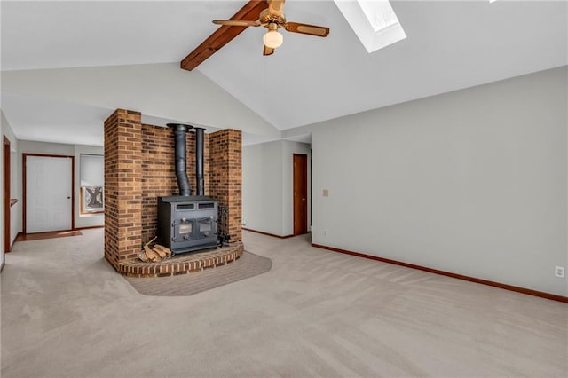 unfurnished living room featuring a ceiling fan, a skylight, carpet flooring, a wood stove, and baseboards