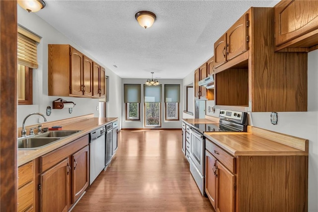 kitchen featuring stainless steel appliances, under cabinet range hood, a sink, a chandelier, and wood finished floors