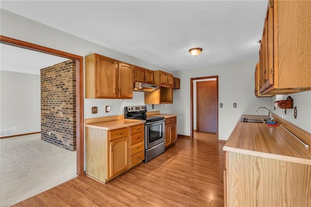 kitchen featuring electric stove, a sink, under cabinet range hood, light countertops, and light wood-type flooring