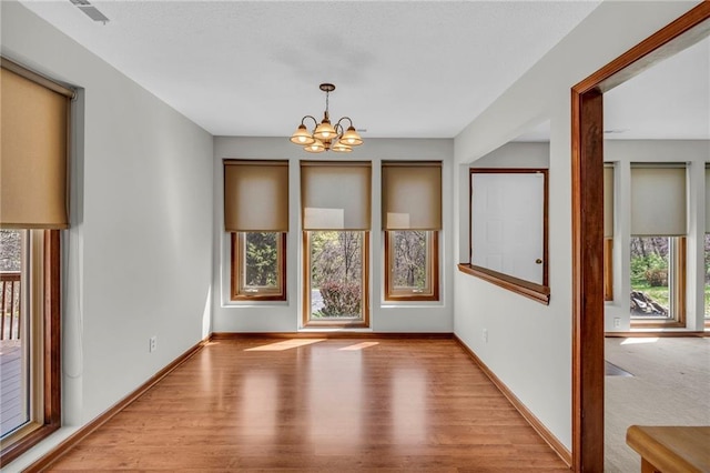 unfurnished dining area with plenty of natural light, a chandelier, wood finished floors, and baseboards