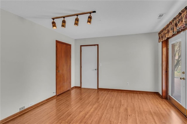 empty room featuring light wood finished floors, baseboards, and track lighting