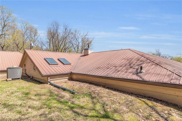 rear view of property featuring central AC, metal roof, and a chimney