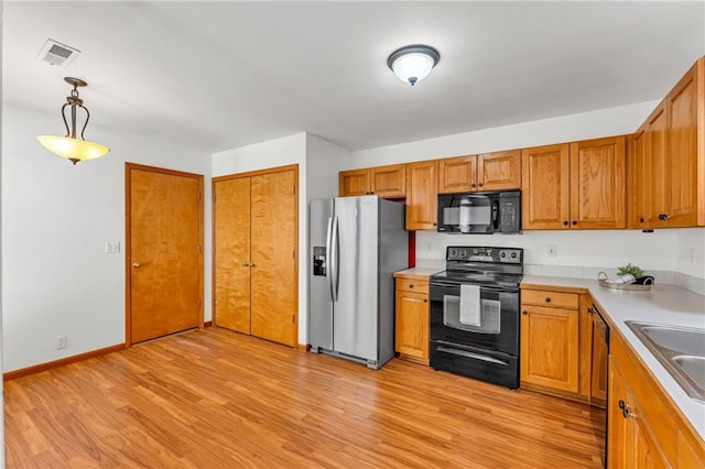 kitchen featuring black appliances, light wood-style flooring, light countertops, pendant lighting, and brown cabinetry