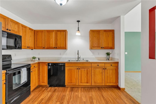kitchen with black appliances, a sink, light countertops, brown cabinetry, and light wood finished floors