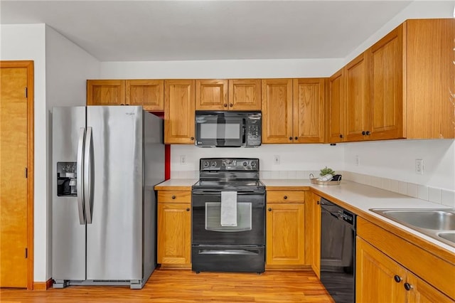 kitchen featuring black appliances, light wood-style flooring, light countertops, and brown cabinets