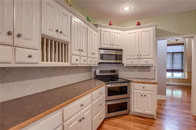 7100 N Cherry St, Gladstone, MO 64118 - kitchen featuring appliances with stainless steel finishes, dark countertops, light wood finished floors, backsplash, and white cabinets