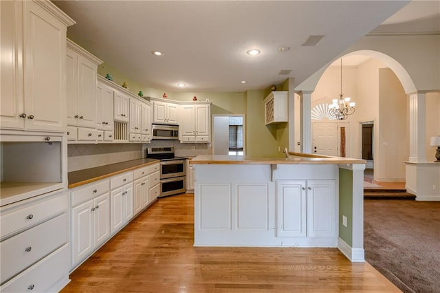 7100 N Cherry St, Gladstone, MO 64118 - kitchen with appliances with stainless steel finishes, a chandelier, arched walkways, tasteful backsplash, and white cabinets