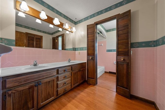 2107 N 154th Ter, Basehor, KS 66007 - bathroom featuring tile walls, double vanity, wood finished floors, a wainscoted wall, and a tub