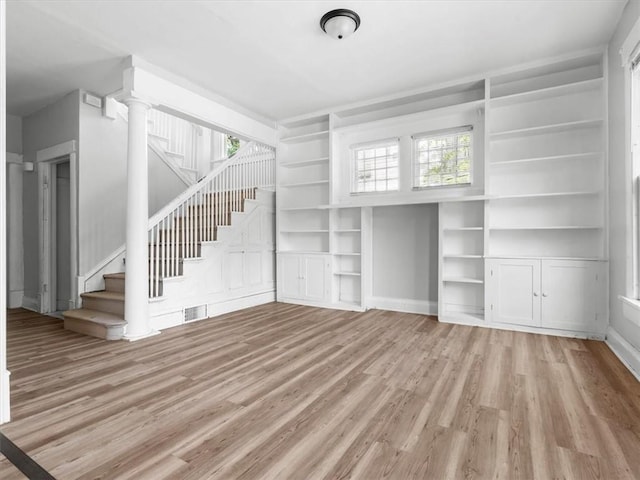 unfurnished living room featuring wood finished floors, stairway, built in features, and decorative columns