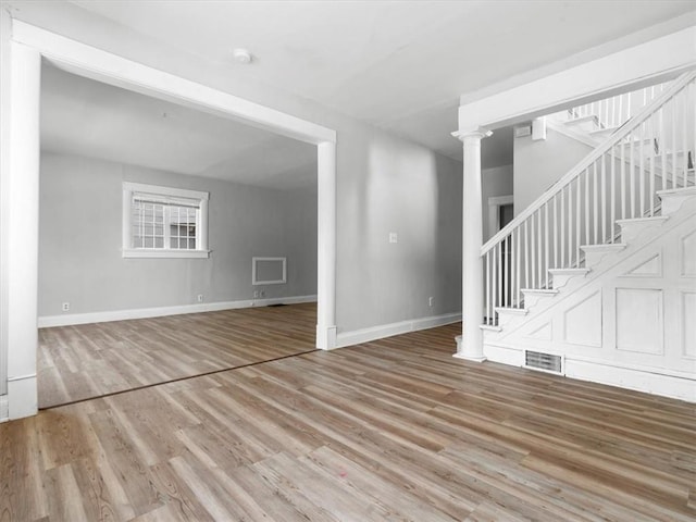 unfurnished living room with stairs, light wood-type flooring, and baseboards