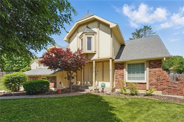 view of front of home featuring a front lawn, stucco siding, a shingled roof, and brick siding