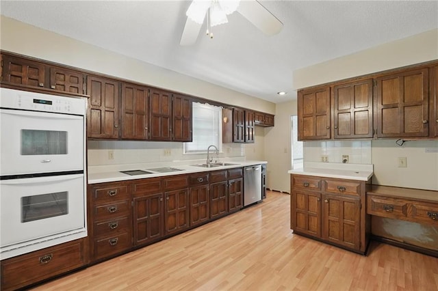 kitchen with a sink, white double oven, dishwasher, light wood-style flooring, and light countertops