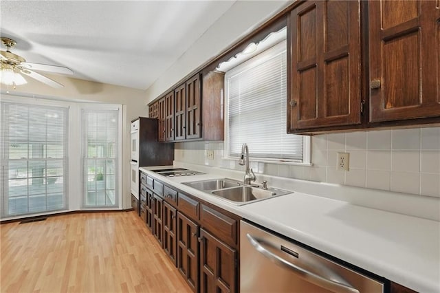 kitchen featuring stainless steel dishwasher, a sink, a ceiling fan, light countertops, and healthy amount of natural light