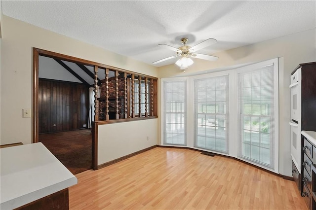 unfurnished dining area with light wood finished floors, ceiling fan, baseboards, and a textured ceiling