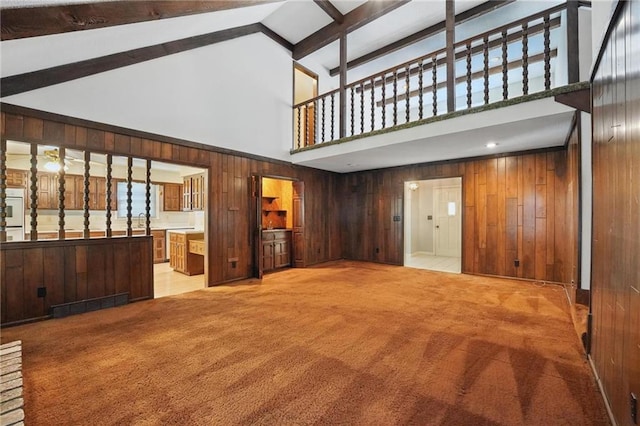 unfurnished living room with high vaulted ceiling, light colored carpet, beamed ceiling, and wood walls