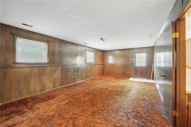 empty room featuring a textured ceiling, plenty of natural light, wooden walls, and carpet