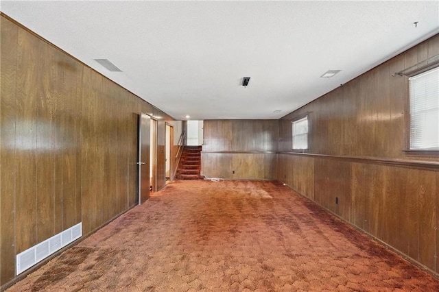 unfurnished room with wooden walls, carpet flooring, and stairway