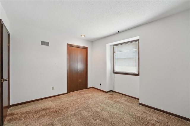 empty room with carpet flooring, baseboards, and a textured ceiling