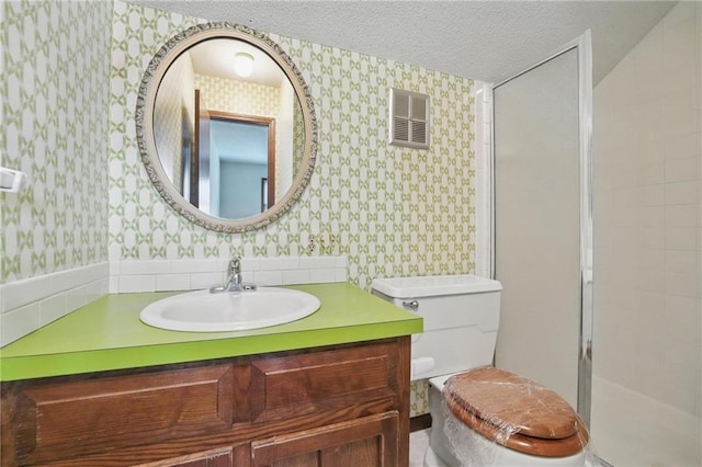 bathroom with wallpapered walls, vanity, a textured ceiling, a stall shower, and toilet