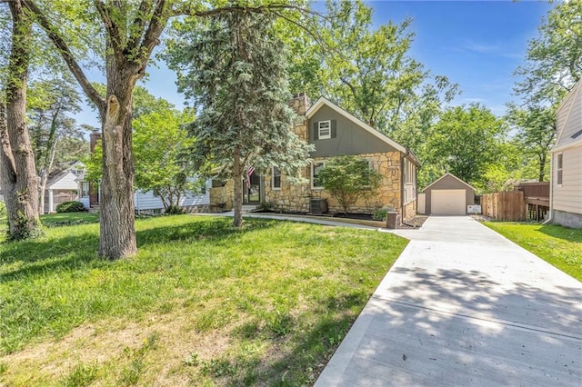 view of property hidden behind natural elements featuring stone siding, a detached garage, driveway, an outbuilding, and a front yard