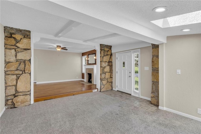 unfurnished living room with carpet, a fireplace, a skylight, baseboards, and a textured ceiling